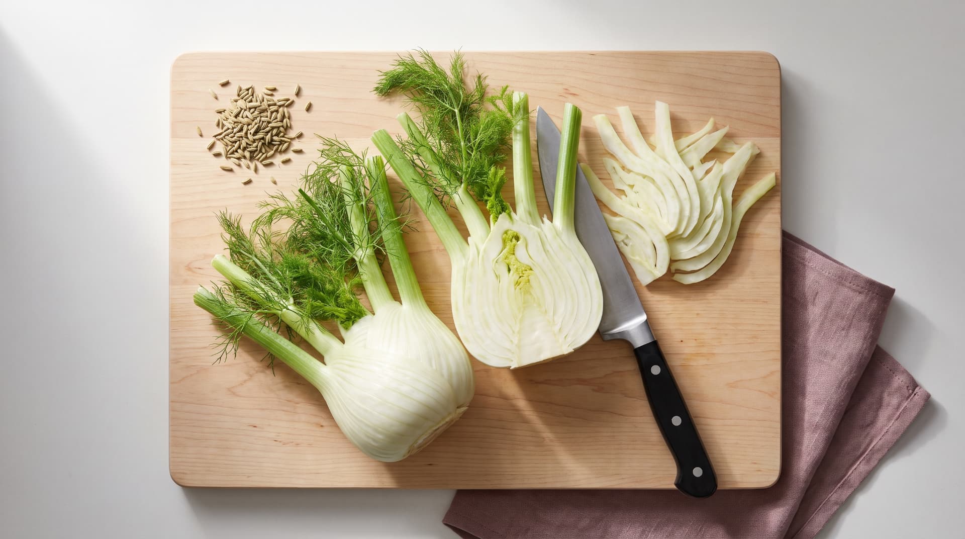 Fresh fennel bulb halved to show the core, with fronds and seeds, on a wood cutting board