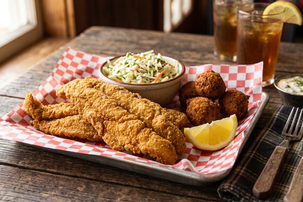 Golden fried fish fillets with a crispy cornmeal crust served with coleslaw, hush puppies, and lemon wedges for a classic fish fry spread
