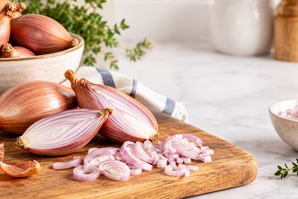 a bowl of Shallots, with some shallots on a cutting board sliced