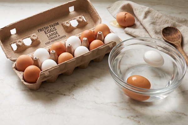 A carton of whole eggs next to a bowl showing the float test, with one cracked egg set aside, illustrating fridge egg storage and spoilage signs