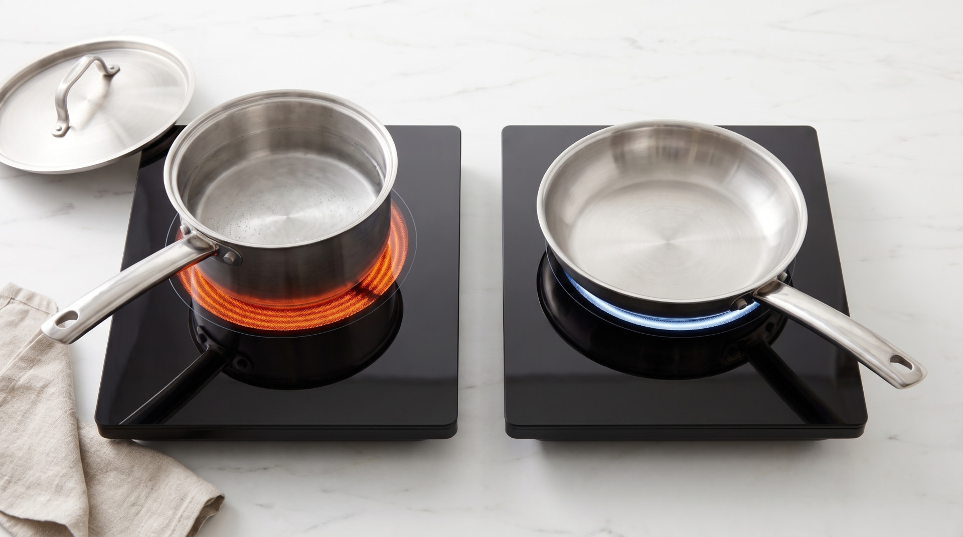 Stainless steel saucepan on a smooth black glass cooktop with a cast iron skillet nearby